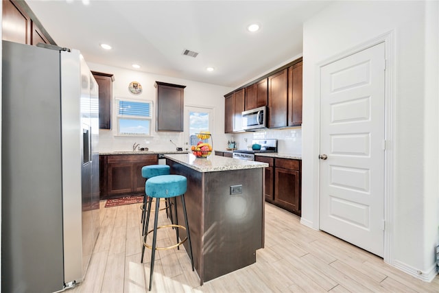 kitchen with decorative backsplash, a center island, light hardwood / wood-style floors, and stainless steel appliances