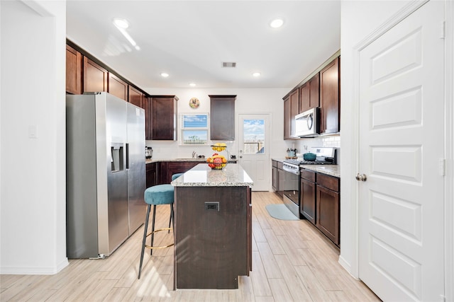 kitchen featuring a breakfast bar, a center island, appliances with stainless steel finishes, and light hardwood / wood-style flooring