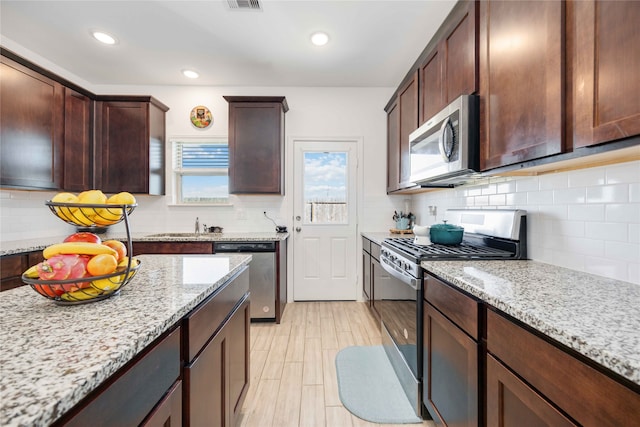 kitchen with dark brown cabinetry, stainless steel appliances, light stone counters, and tasteful backsplash