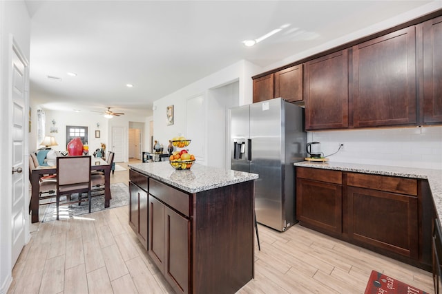 kitchen featuring stainless steel fridge with ice dispenser, light wood-type flooring, a center island, and light stone counters