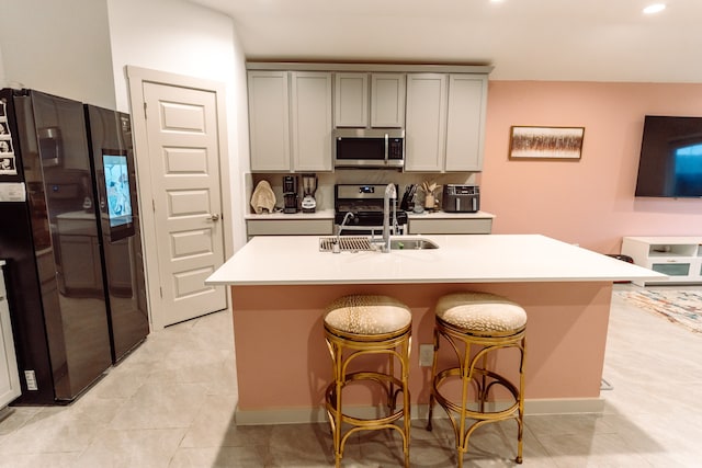 kitchen with gray cabinetry, sink, a breakfast bar area, a center island with sink, and appliances with stainless steel finishes