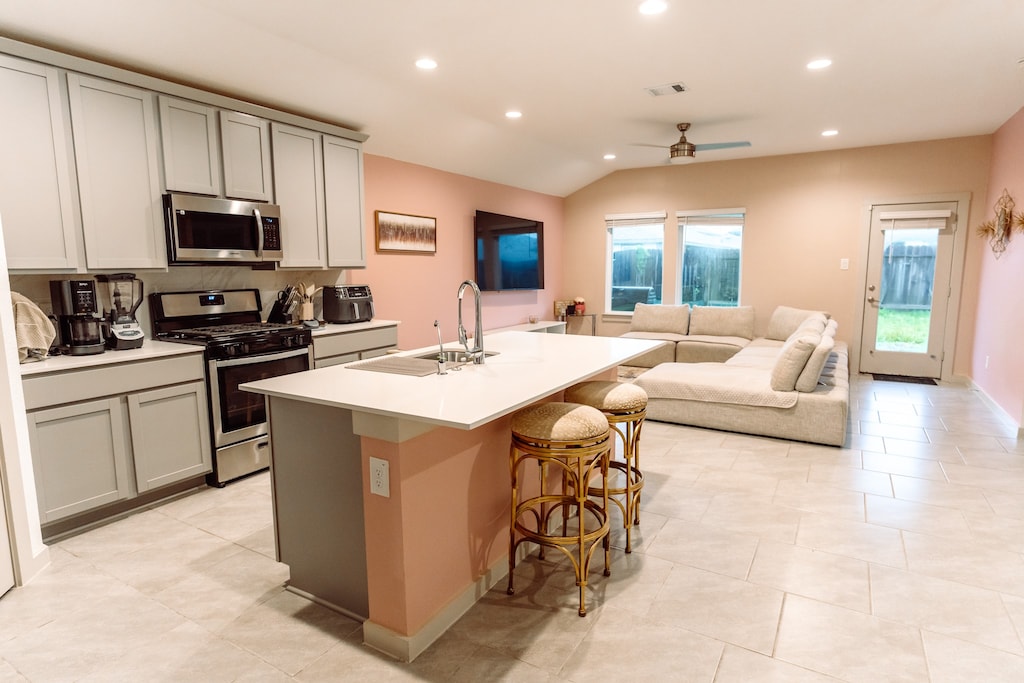 kitchen with gray cabinets, vaulted ceiling, stainless steel appliances, and an island with sink