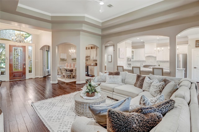 living room with crown molding, dark hardwood / wood-style flooring, a high ceiling, and an inviting chandelier