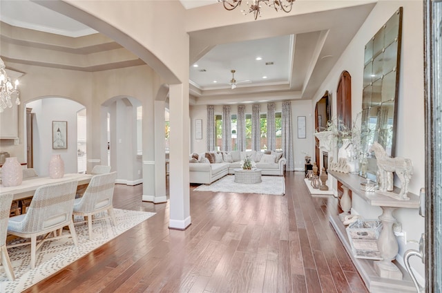 foyer entrance with hardwood / wood-style flooring, ceiling fan with notable chandelier, crown molding, and a tray ceiling