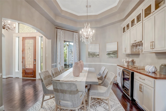 dining room featuring dark wood-type flooring, an inviting chandelier, a raised ceiling, crown molding, and beverage cooler