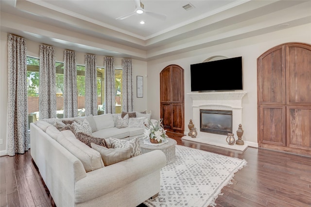 living room with dark hardwood / wood-style floors, crown molding, ceiling fan, and a tray ceiling