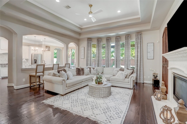 living room featuring ceiling fan with notable chandelier, dark hardwood / wood-style floors, a raised ceiling, and crown molding