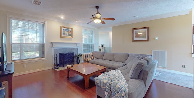 living room featuring a tiled fireplace, ceiling fan, hardwood / wood-style floors, and crown molding