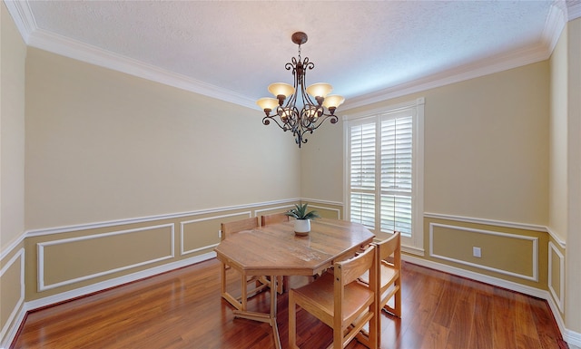 dining area featuring ornamental molding, wood-type flooring, a textured ceiling, and an inviting chandelier