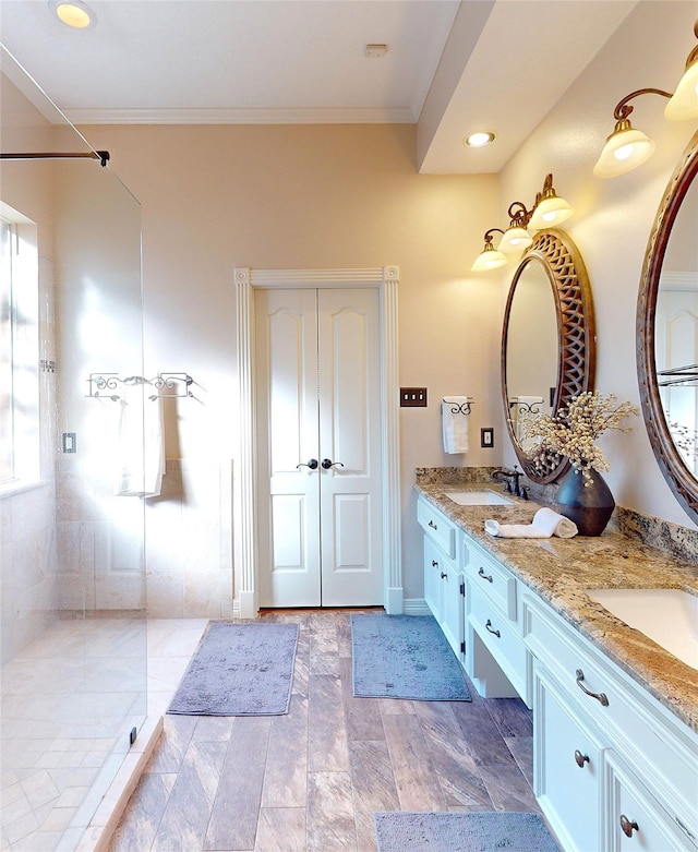 bathroom with tiled shower, hardwood / wood-style flooring, vanity, and ornamental molding