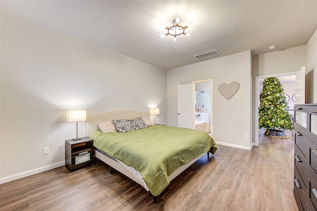 bedroom featuring ensuite bathroom, wood-type flooring, and a textured ceiling