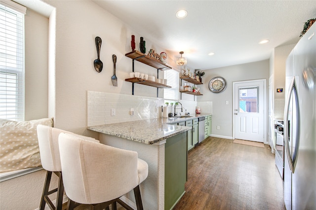 kitchen with decorative backsplash, stainless steel appliances, a breakfast bar area, dark hardwood / wood-style floors, and green cabinets