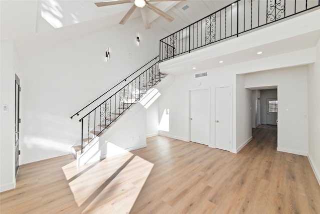 stairs with hardwood / wood-style floors, ceiling fan, and high vaulted ceiling