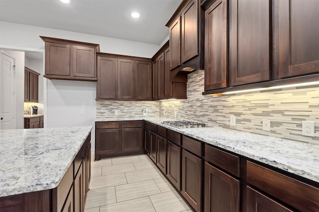 kitchen featuring decorative backsplash, dark brown cabinetry, light stone counters, and stainless steel gas stovetop