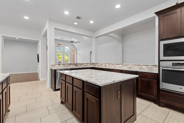 kitchen with light stone countertops, tasteful backsplash, stainless steel oven, ceiling fan, and a kitchen island