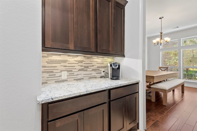 kitchen featuring backsplash, dark brown cabinetry, light stone countertops, and a chandelier