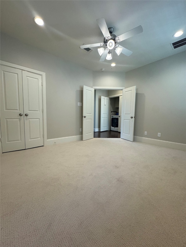 unfurnished bedroom featuring washer / dryer, a closet, light colored carpet, and ceiling fan