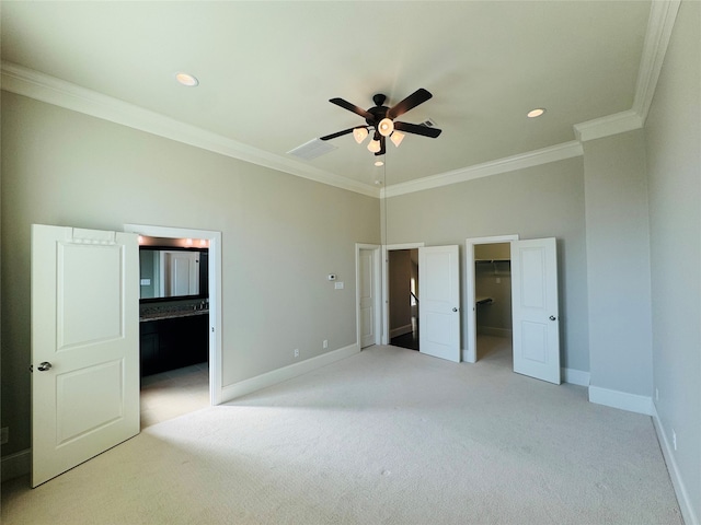 unfurnished bedroom featuring ensuite bathroom, a walk in closet, ceiling fan, ornamental molding, and light colored carpet