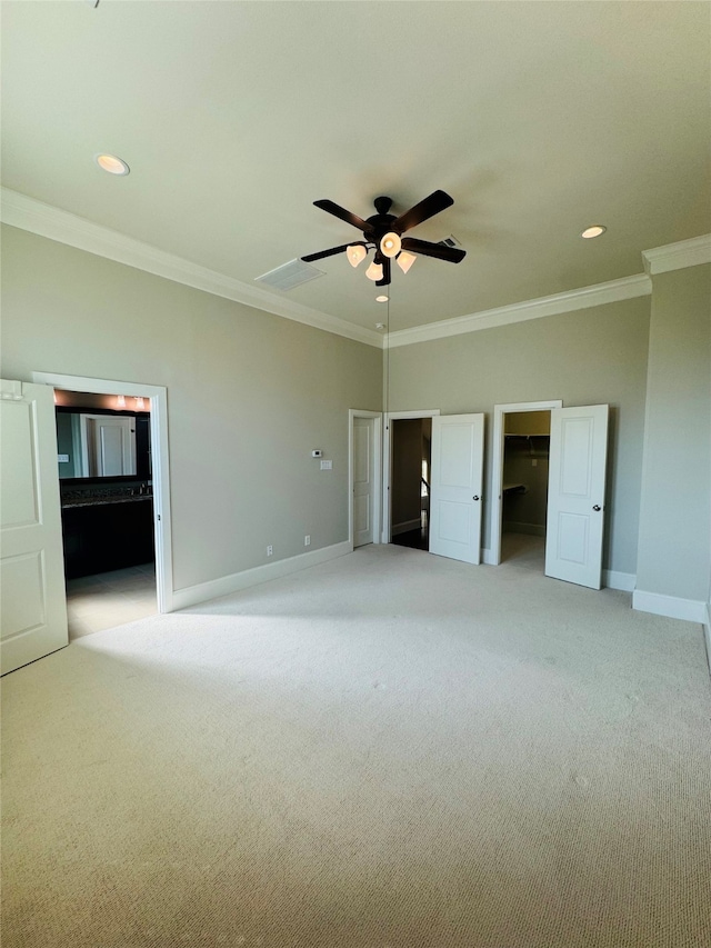 unfurnished bedroom with a walk in closet, light carpet, crown molding, and ceiling fan