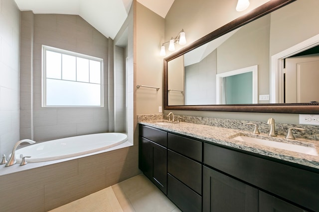 bathroom featuring tile patterned floors, vanity, a relaxing tiled tub, and vaulted ceiling