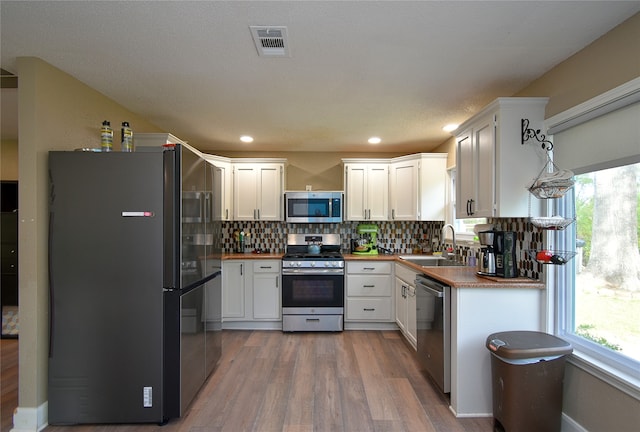 kitchen with decorative backsplash, stainless steel appliances, sink, white cabinets, and hardwood / wood-style floors