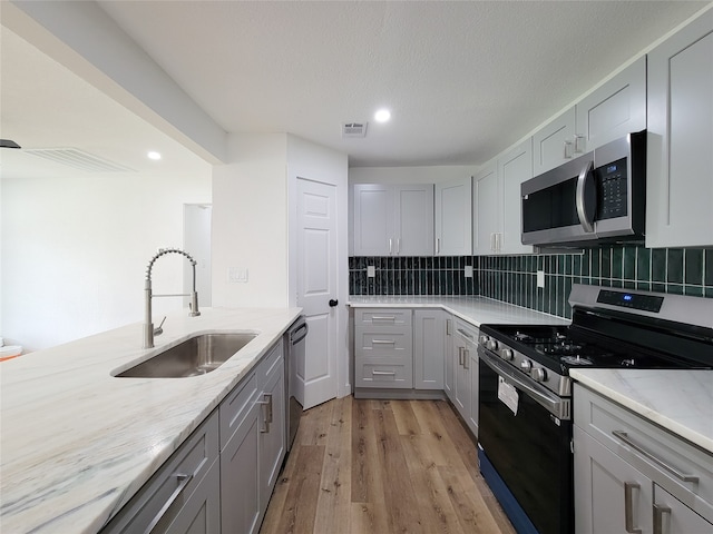 kitchen with appliances with stainless steel finishes, light wood-type flooring, tasteful backsplash, and sink