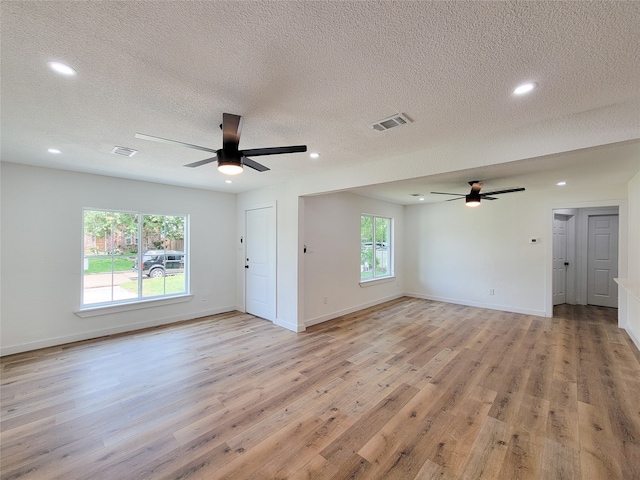 unfurnished living room with a textured ceiling, a wealth of natural light, and light hardwood / wood-style flooring