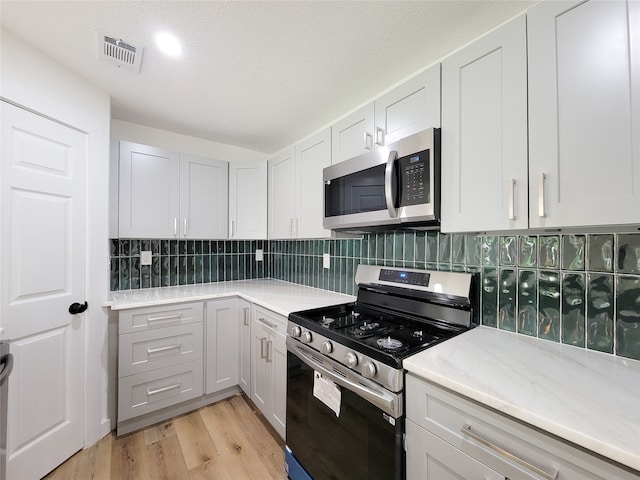 kitchen with appliances with stainless steel finishes, light wood-type flooring, tasteful backsplash, a textured ceiling, and white cabinets