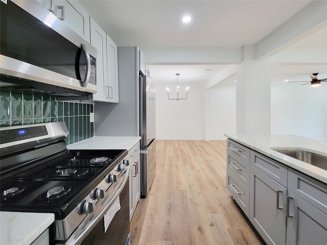 kitchen with gray cabinets, tasteful backsplash, light hardwood / wood-style floors, light stone counters, and stainless steel appliances