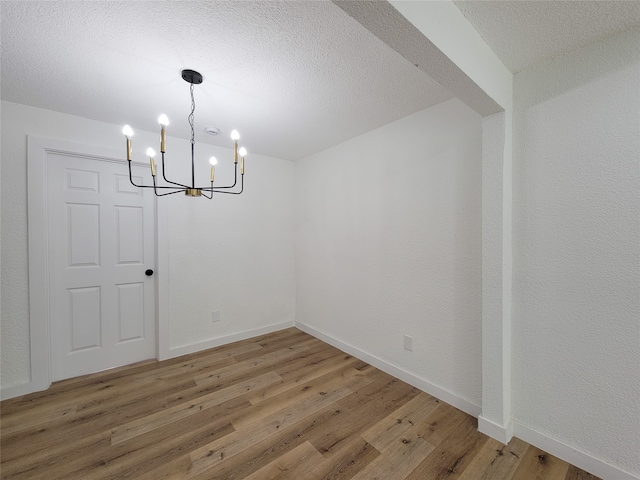 unfurnished dining area with hardwood / wood-style flooring, a textured ceiling, and a chandelier