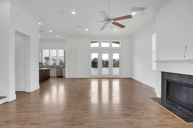 unfurnished living room featuring wood-type flooring, a wealth of natural light, crown molding, and a tiled fireplace