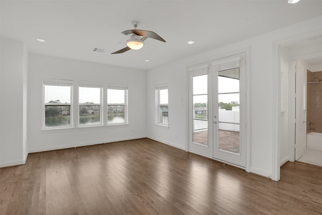 unfurnished living room featuring a water view, plenty of natural light, dark wood-type flooring, and ceiling fan