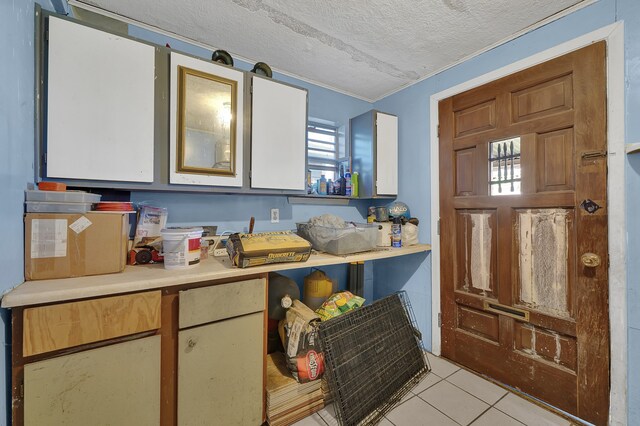 kitchen with white cabinets, light tile patterned floors, a textured ceiling, and ornamental molding