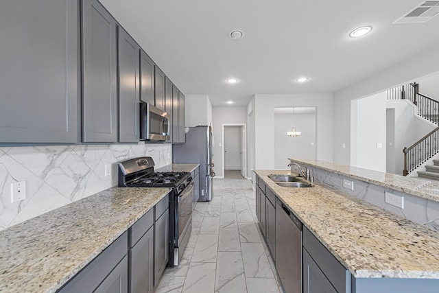 kitchen with an island with sink, sink, backsplash, stainless steel appliances, and light stone countertops