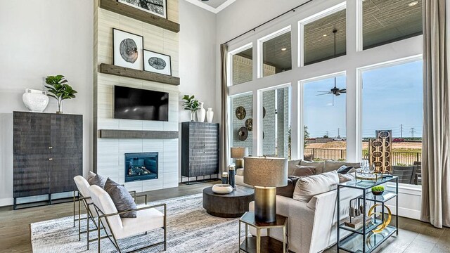 living room with ceiling fan, a high ceiling, hardwood / wood-style floors, a fireplace, and ornamental molding