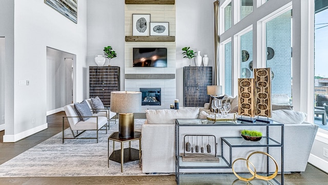 living room featuring a wealth of natural light, a large fireplace, a towering ceiling, and dark hardwood / wood-style floors