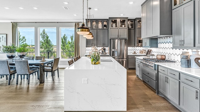 kitchen featuring dark hardwood / wood-style flooring, stainless steel appliances, wall chimney range hood, pendant lighting, and an island with sink