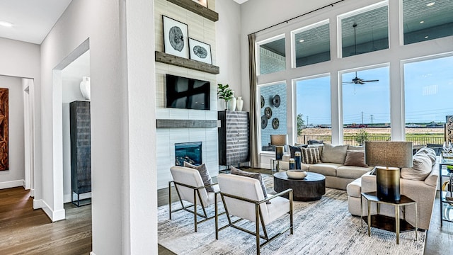 living room featuring a tiled fireplace, ceiling fan, a towering ceiling, and wood-type flooring