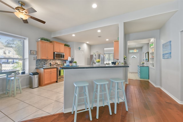 kitchen featuring a breakfast bar, stainless steel appliances, light hardwood / wood-style flooring, and ceiling fan