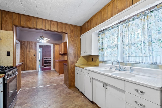 kitchen with stainless steel range with gas cooktop, wooden walls, white cabinets, and ceiling fan