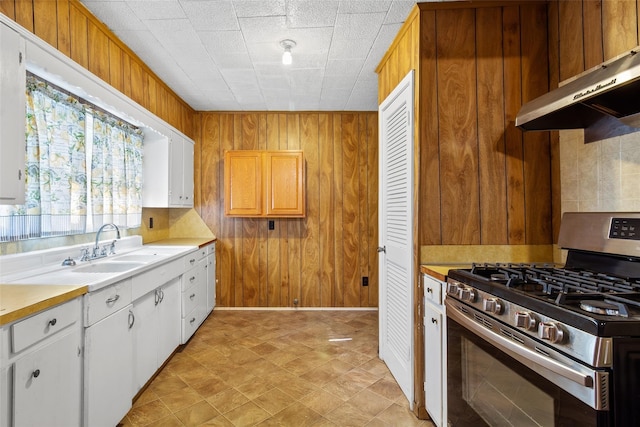 kitchen featuring decorative backsplash, exhaust hood, white cabinets, stainless steel range with gas stovetop, and wood walls