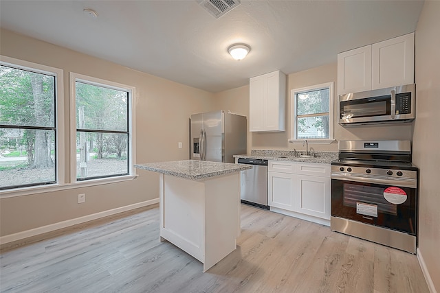 kitchen with a center island, light stone countertops, light wood-type flooring, appliances with stainless steel finishes, and white cabinetry