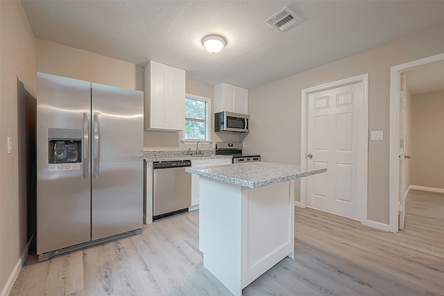 kitchen featuring white cabinets, a kitchen island, a textured ceiling, light hardwood / wood-style floors, and stainless steel appliances