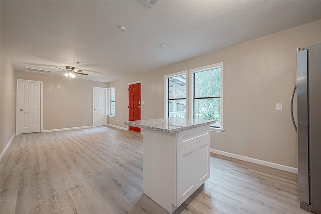 kitchen with light wood-type flooring, ceiling fan, white cabinets, a kitchen island, and stainless steel refrigerator