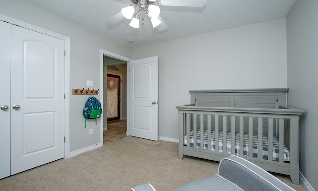 carpeted bedroom with a nursery area, a textured ceiling, and ceiling fan