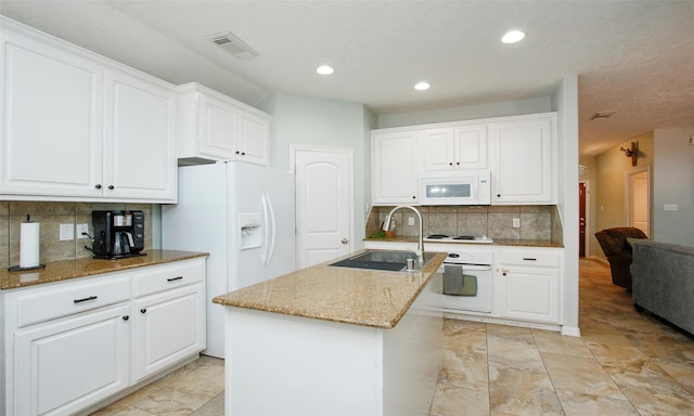 kitchen with sink, white cabinets, a kitchen island with sink, light stone countertops, and white appliances