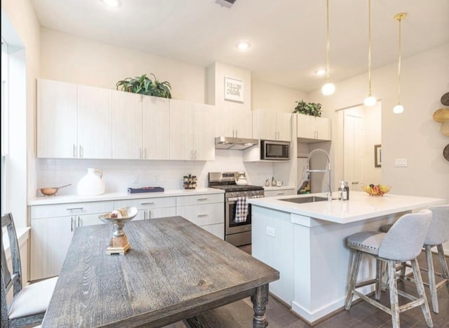 kitchen with hanging light fixtures, white cabinetry, a kitchen island with sink, and appliances with stainless steel finishes