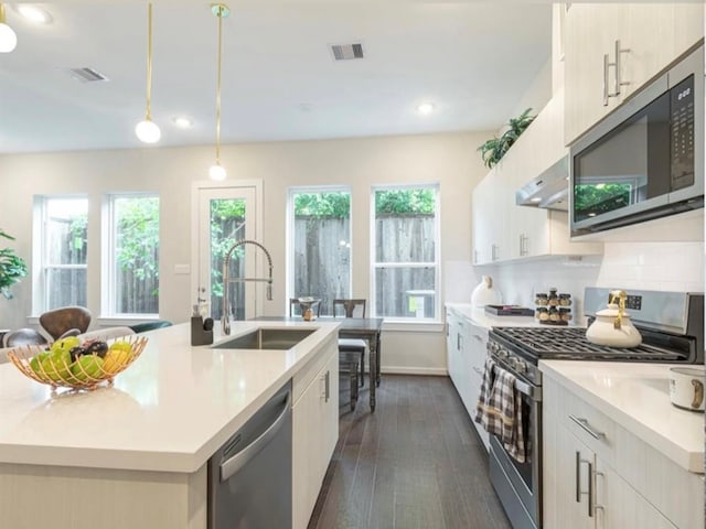 kitchen with sink, stainless steel appliances, dark hardwood / wood-style flooring, decorative light fixtures, and a center island with sink