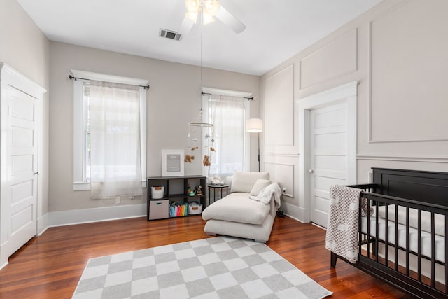 bedroom featuring ceiling fan, wood-type flooring, and a crib