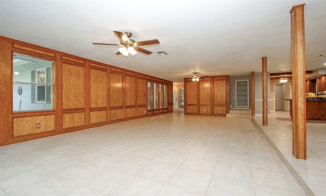 unfurnished room with a textured ceiling, ceiling fan, and wooden walls